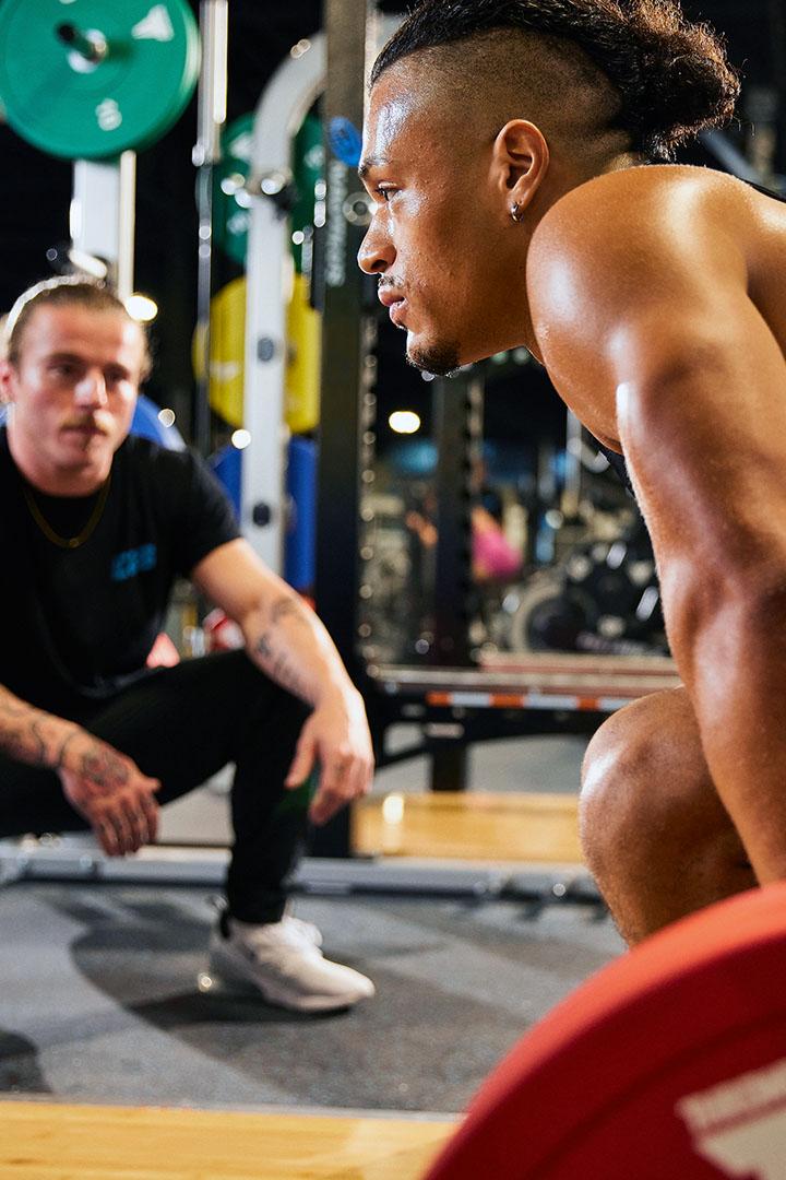 Trainer observing and motivating a man performing a heavy lift in the gym