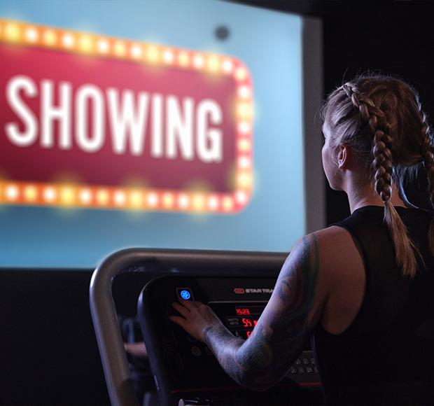 eos gym member on a tredmill watching a movie displayed on a large screen