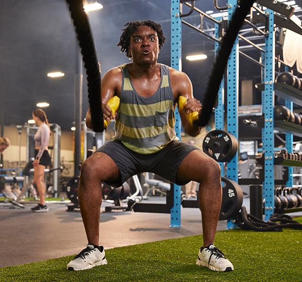 eos gym member in tank top using the battle ropes