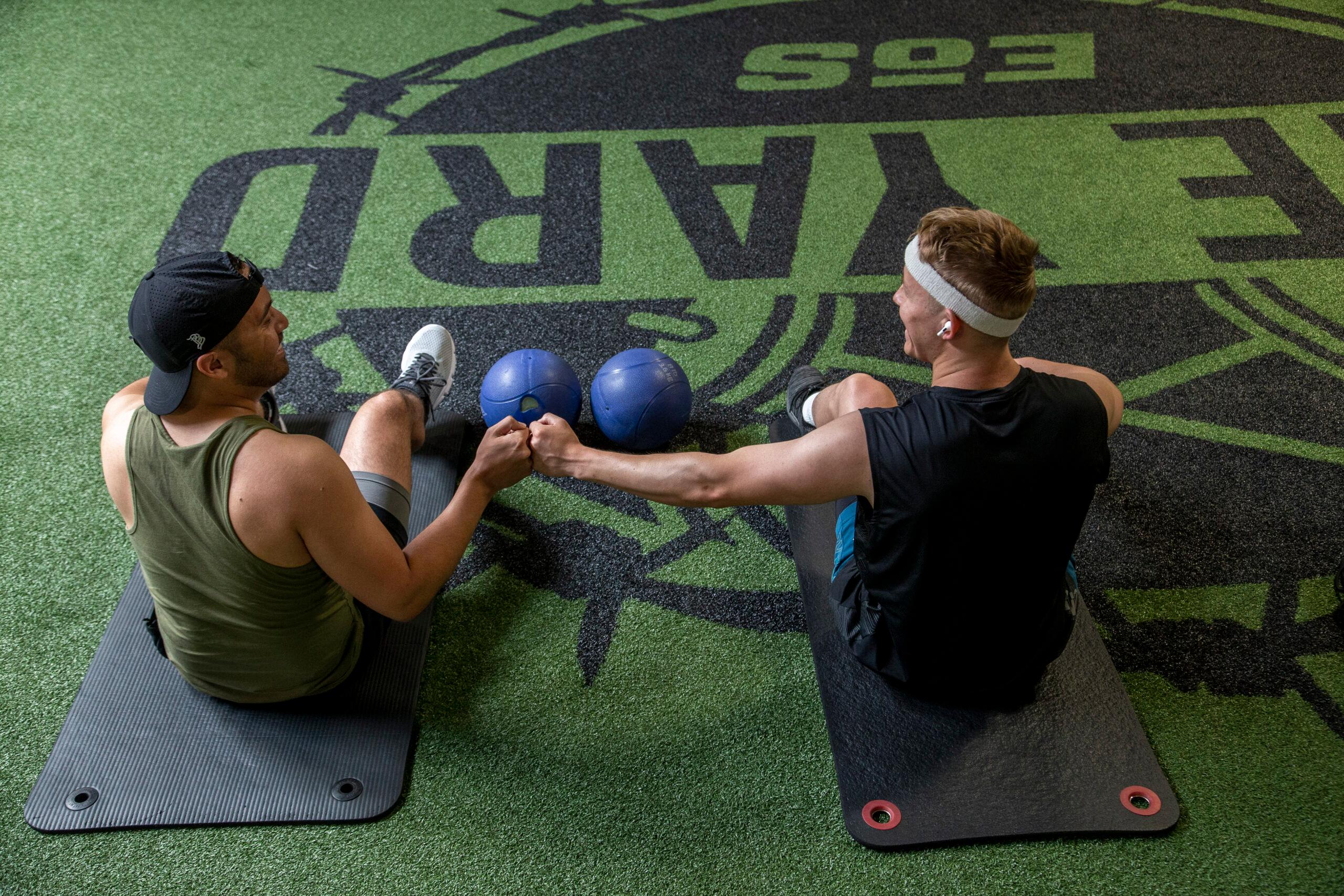 two eos gym members sitting on yoga mats inside a eos branded gym fist bumping