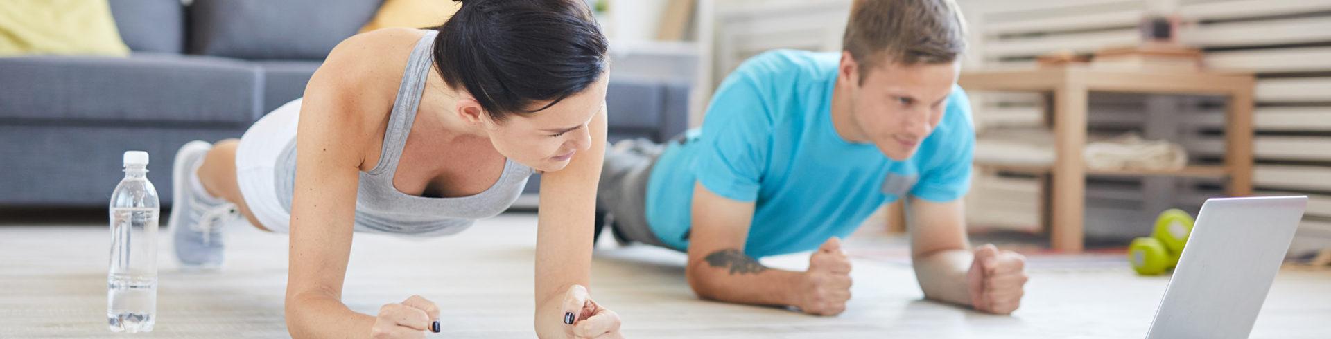 an athletic couple doing planks together in a clean living room